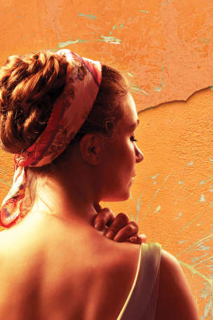 Woman with hair in a braided bun and floral headband facing towards a wall that's textured orange wall with paint splatters in leaf-like patterns