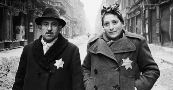 A Jewish man and woman on an empty street looking at the camera with yellow stars on their coats