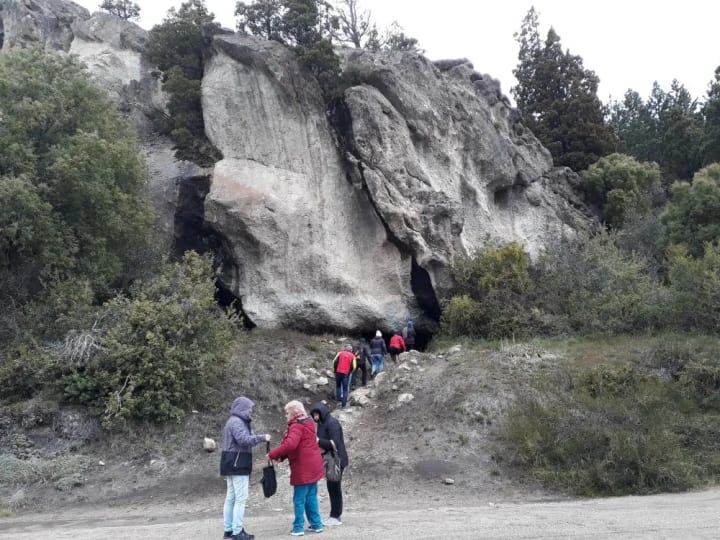 El paredón de la Casa de Piedra con su alero, y un grupo de visitantes subiendo por el sendero