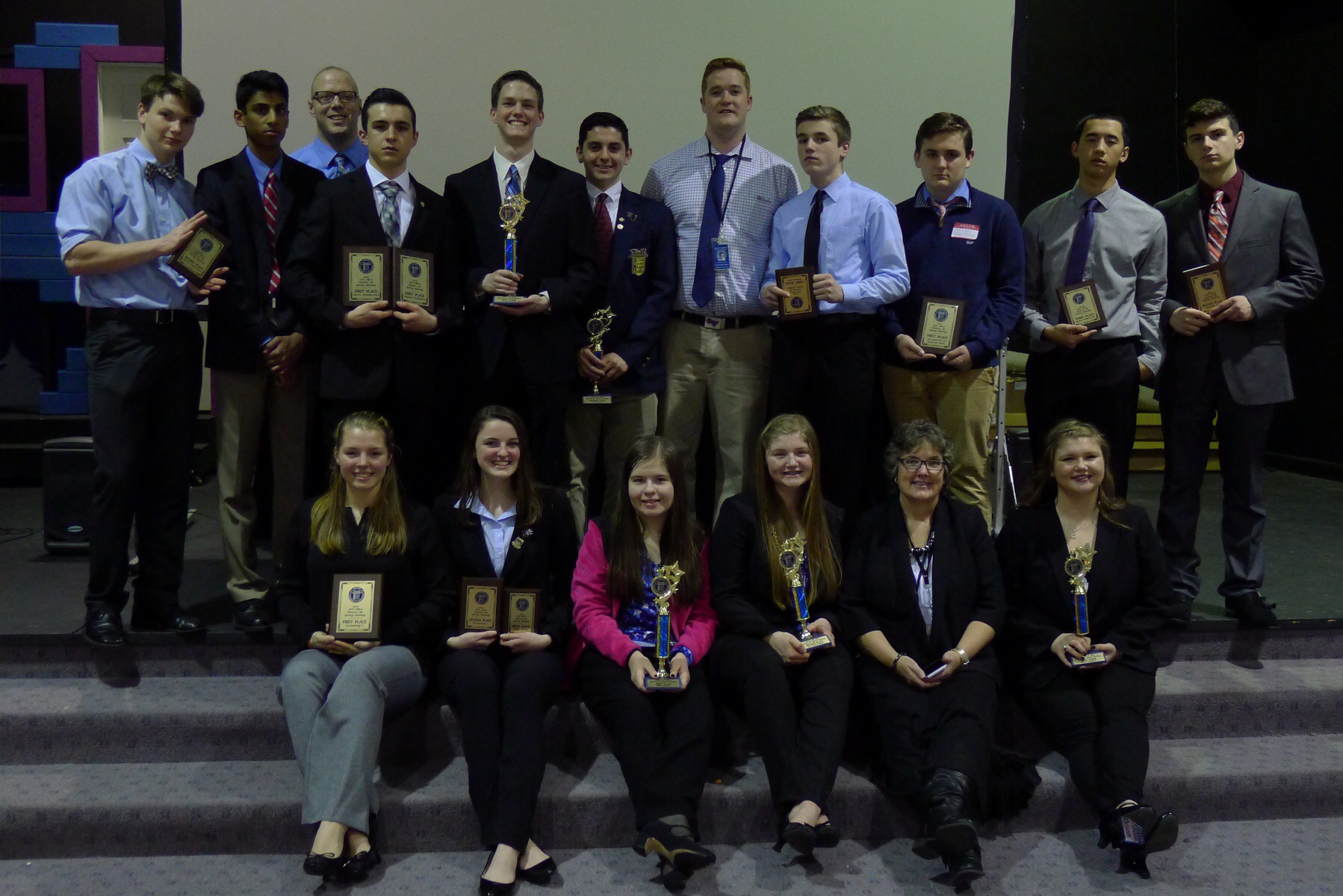 Students sit on a stair case holding awards 