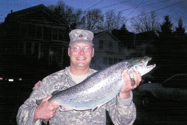 Staff Sergeant Ryan Claxton holds an Atlantic salmon he caught while fishing from the shore of the Oswego River in downtown