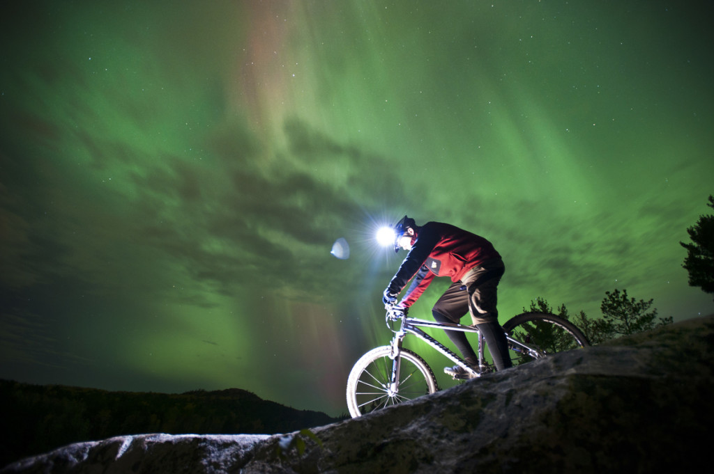 Night mountain bike riding with aurora borealis northern lights near Marquette Michigan.