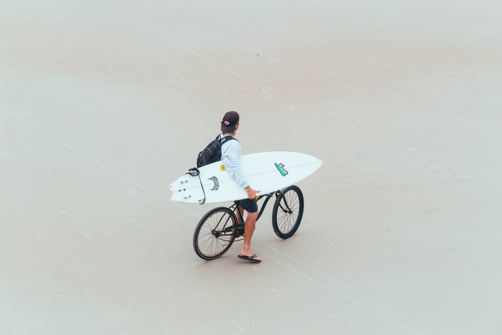 A man carries a surfboard on a bike in Daytona Beach.