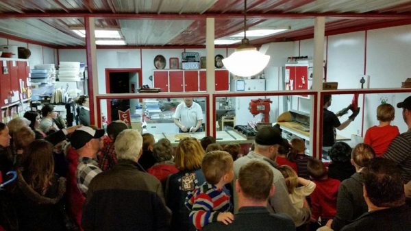 A crowd of all ages is gathered to watch hand made candy canes being made. 