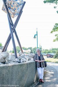 woman leans on concrete wall next to contemporary steel sculpture