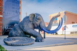 large bronze mastodon sculpture rising from manhole cover