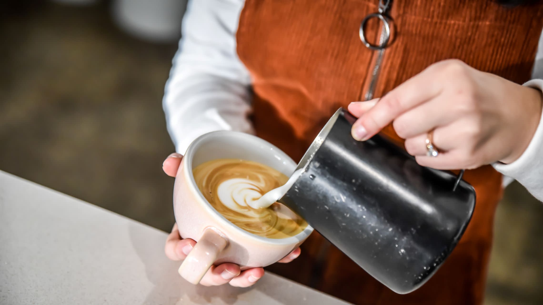 barista pouring milk into coffee