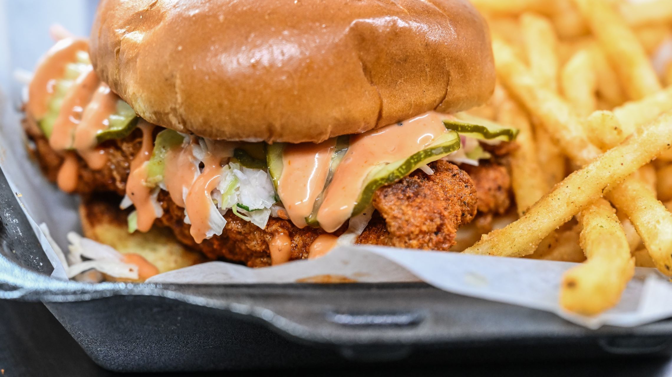 spicy chicken sandwich topped with pickles, slaw and special sauce next to fries
