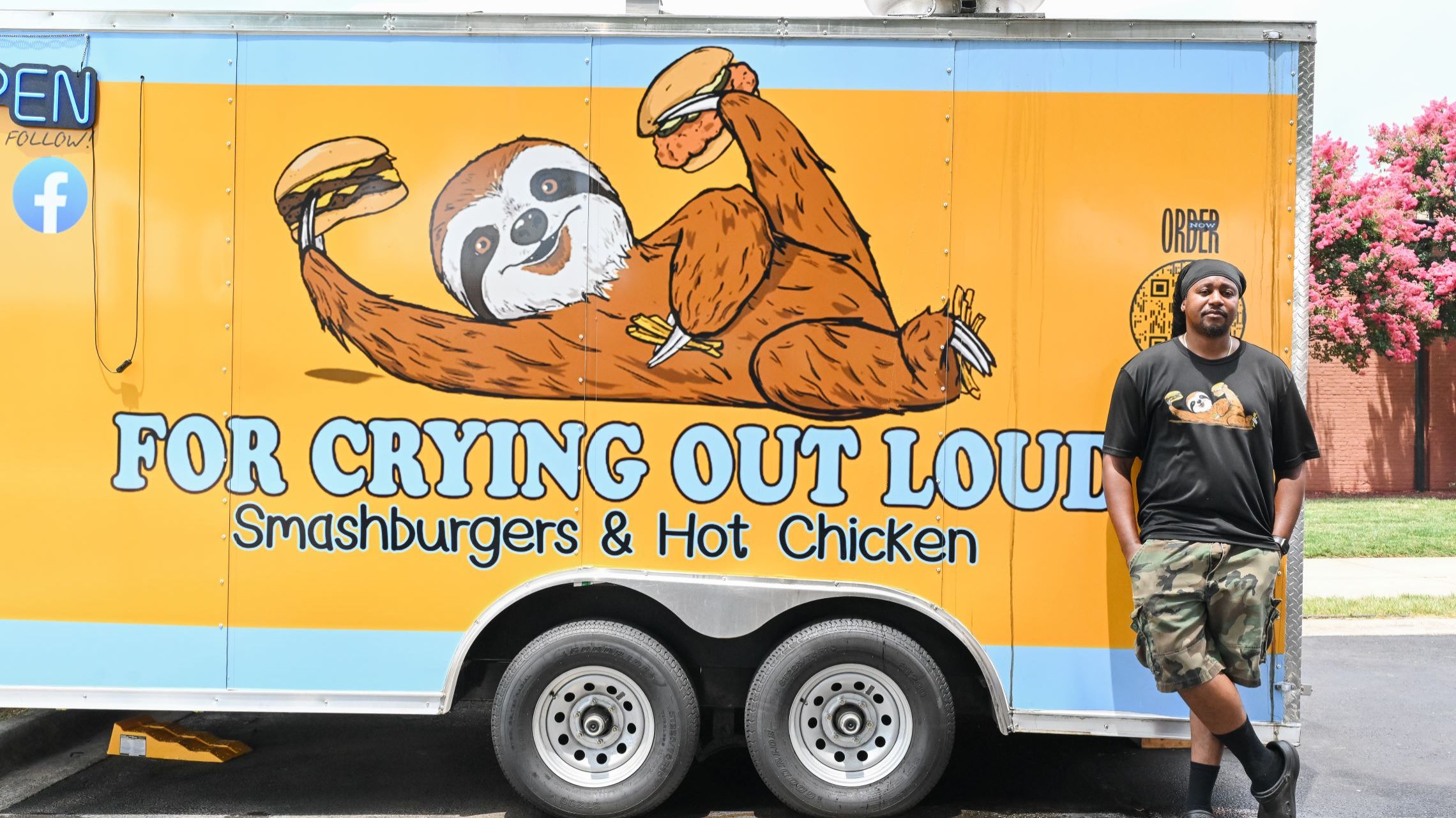 chef stands next to blue and yellow food truck with sloth logo