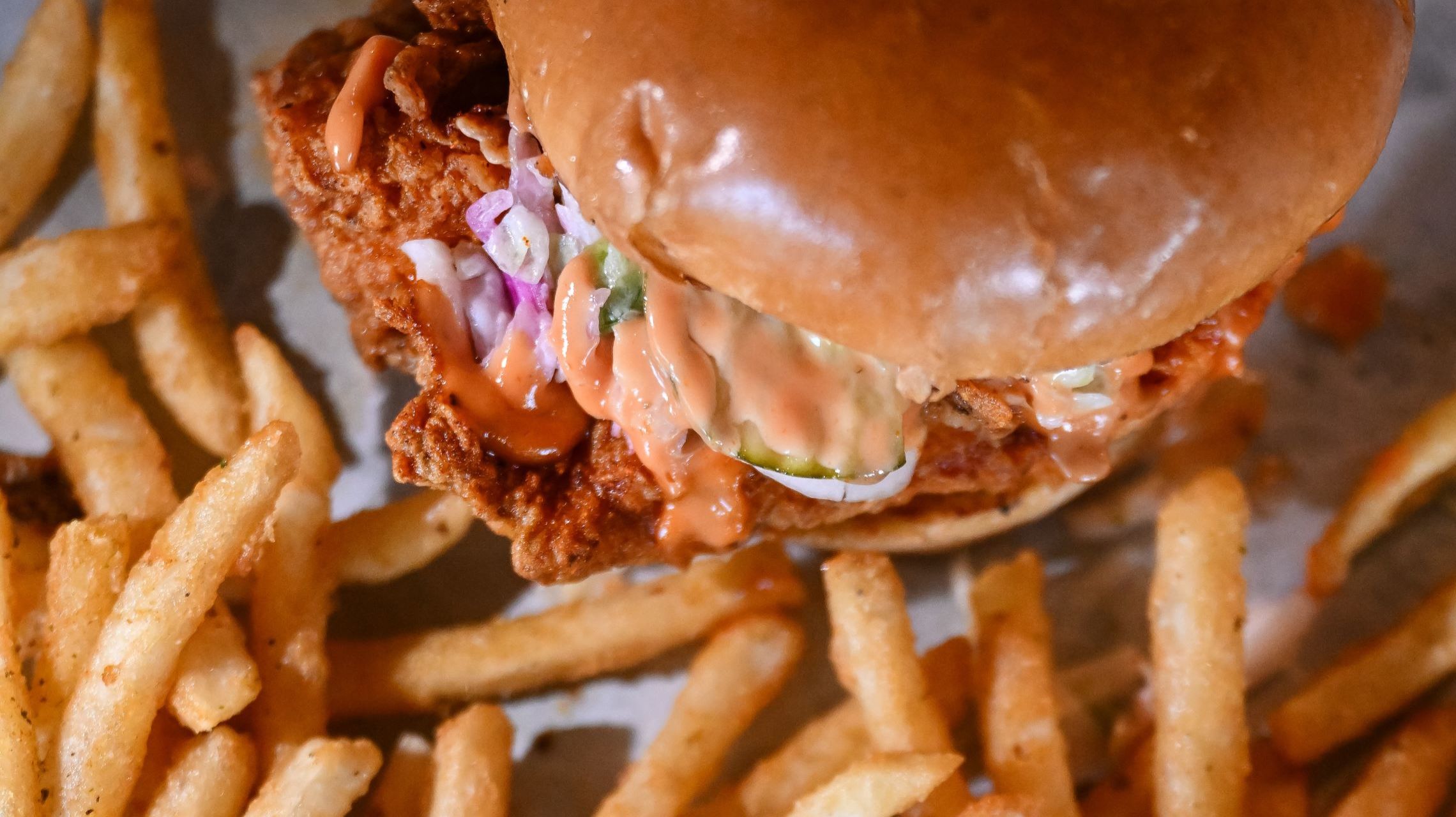 spicy chicken sandwich topped with pickles and slaw next to fries
