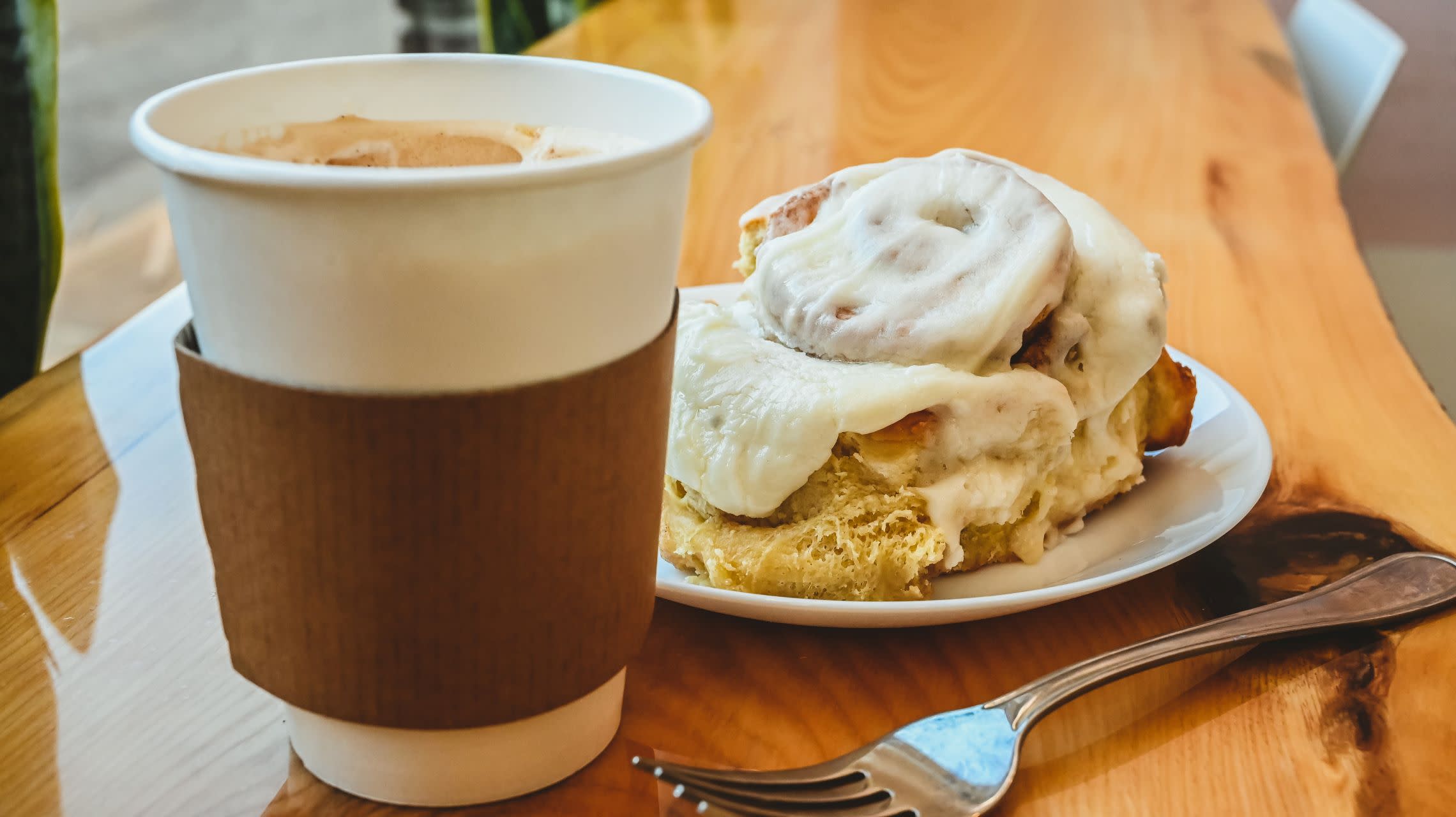 cup of coffee on table with cinnamon roll and fork