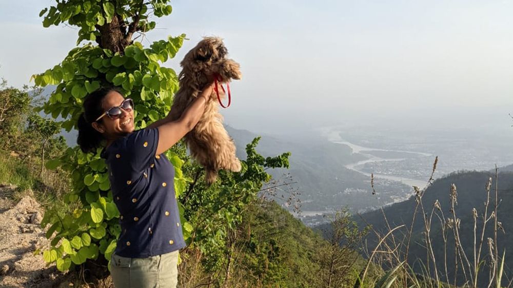 a women holding a dog up high with valley view of rishikesh in the background - Kothli Hills, Rishikesh