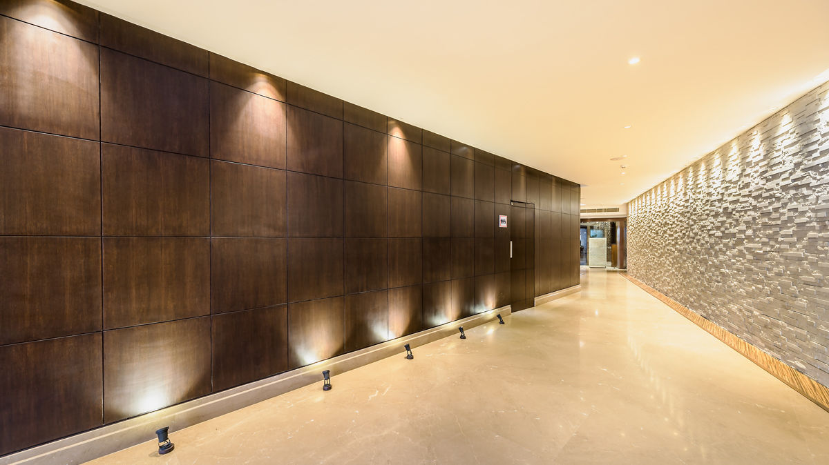 An expansive hotel hallway with wood paneling on one side and a textured silver wall on the other - TGI Grand Fortuna, Hosur
