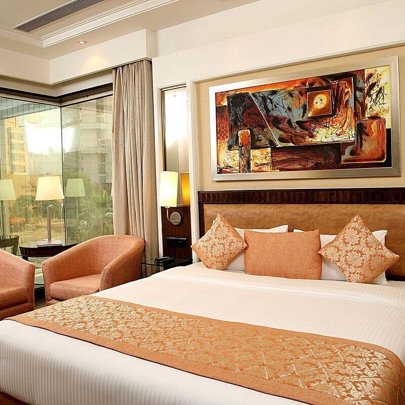 Executive Room with a double bed, bedside table with a lamp on top, cushioned seating with a table in front, and a window behind at Inde Signature Tower, Gurgaon