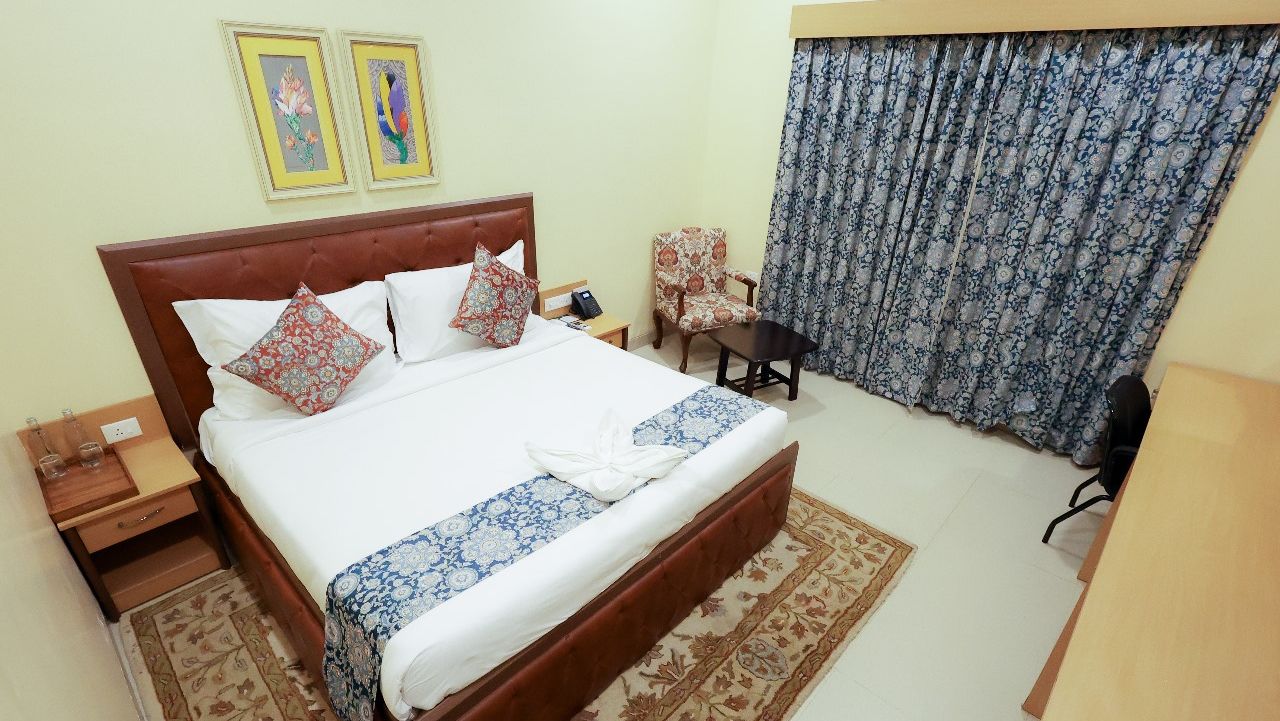 Elegant Deluxe Room at Mayfair World Cup Village, Rourkela, featuring a comfortable bed with patterned decor.