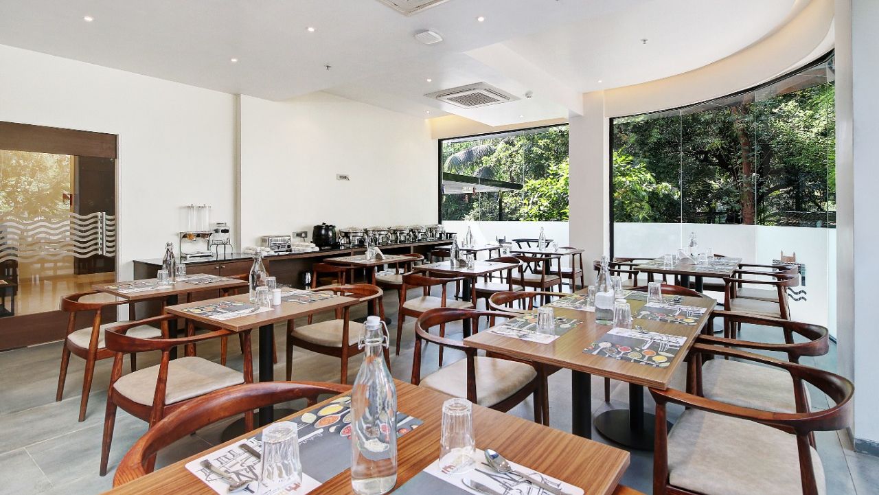 Well lit restaurant area at Hotel Mumbai House, Ghansoli with wooden tables and chairs