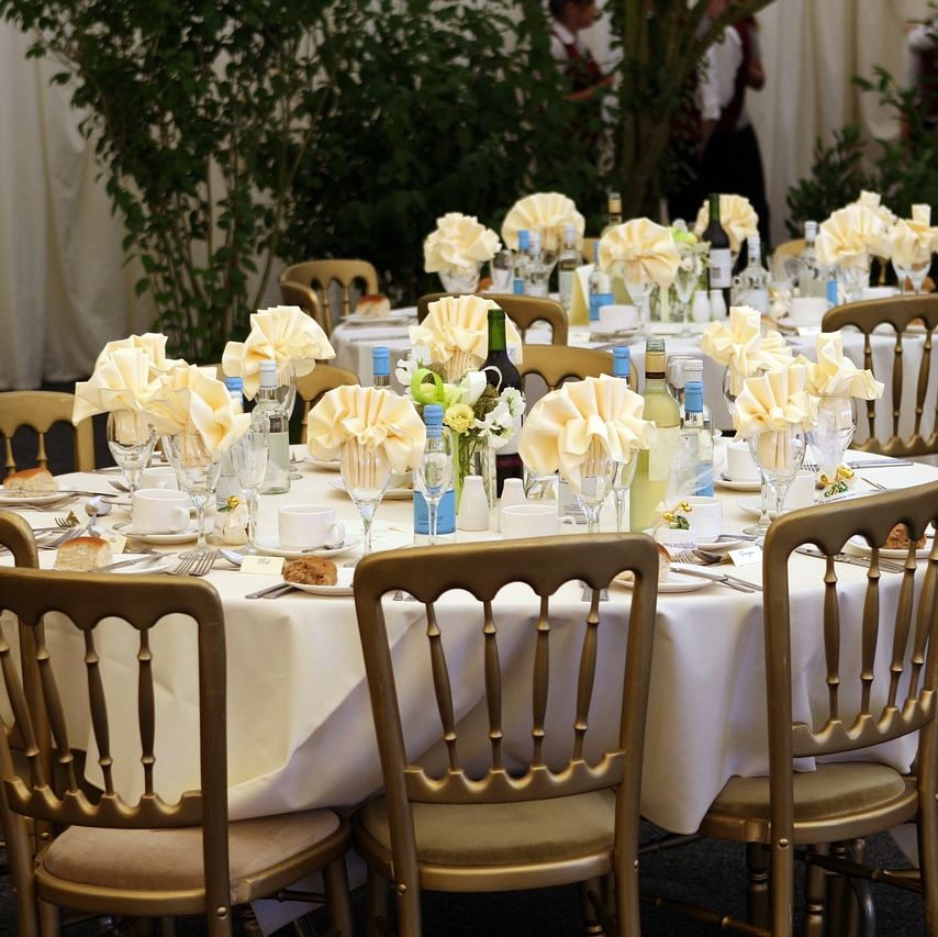 Round banquet tables with white cloths, golden chairs, and cream napkins, adorned with small floral centerpieces and set with dinnerware.