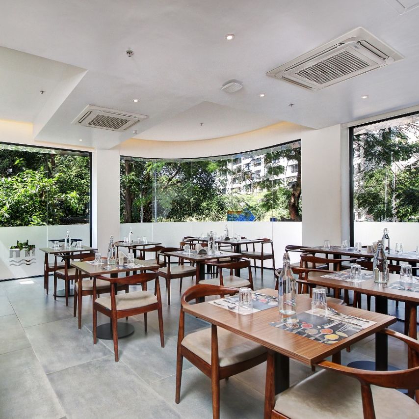 Well lit restaurant area at Hotel Mumbai House, Ghansoli with wooden tables and chairs