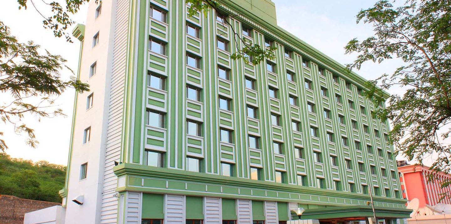 A multi-story green hotel building flanked by trees. - Tara - Comfort Hotel