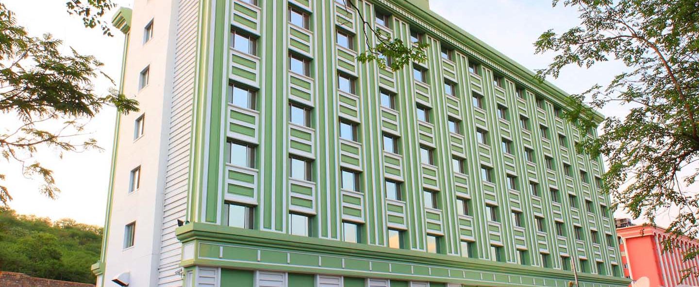 A multi-story green hotel building flanked by trees. - Tara - Comfort Hotel