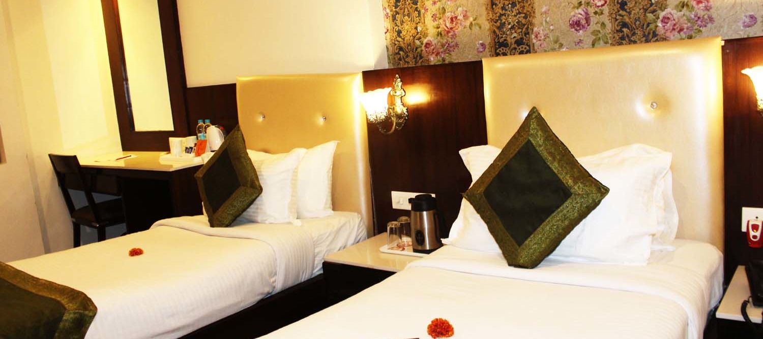 A cosy hotel room with two single beds, beige headboards and a work desk - TGI Apple Inn, Jaipur 