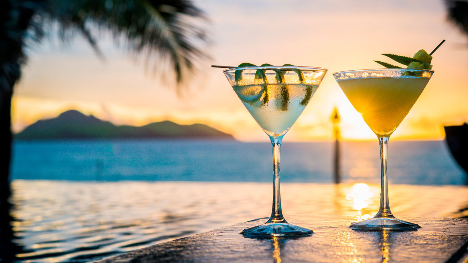 Two refreshing cocktails on a table with a breathtaking sunset view over the ocean in the background.