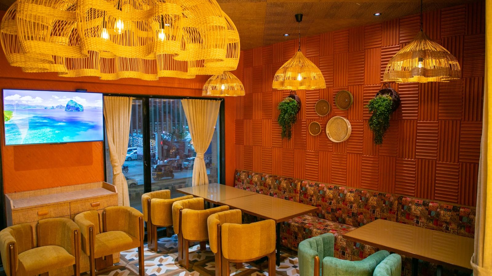 Hotel interior with woven basket-style chandeliers, colorful furniture, and a seaside landscape on a television screen.