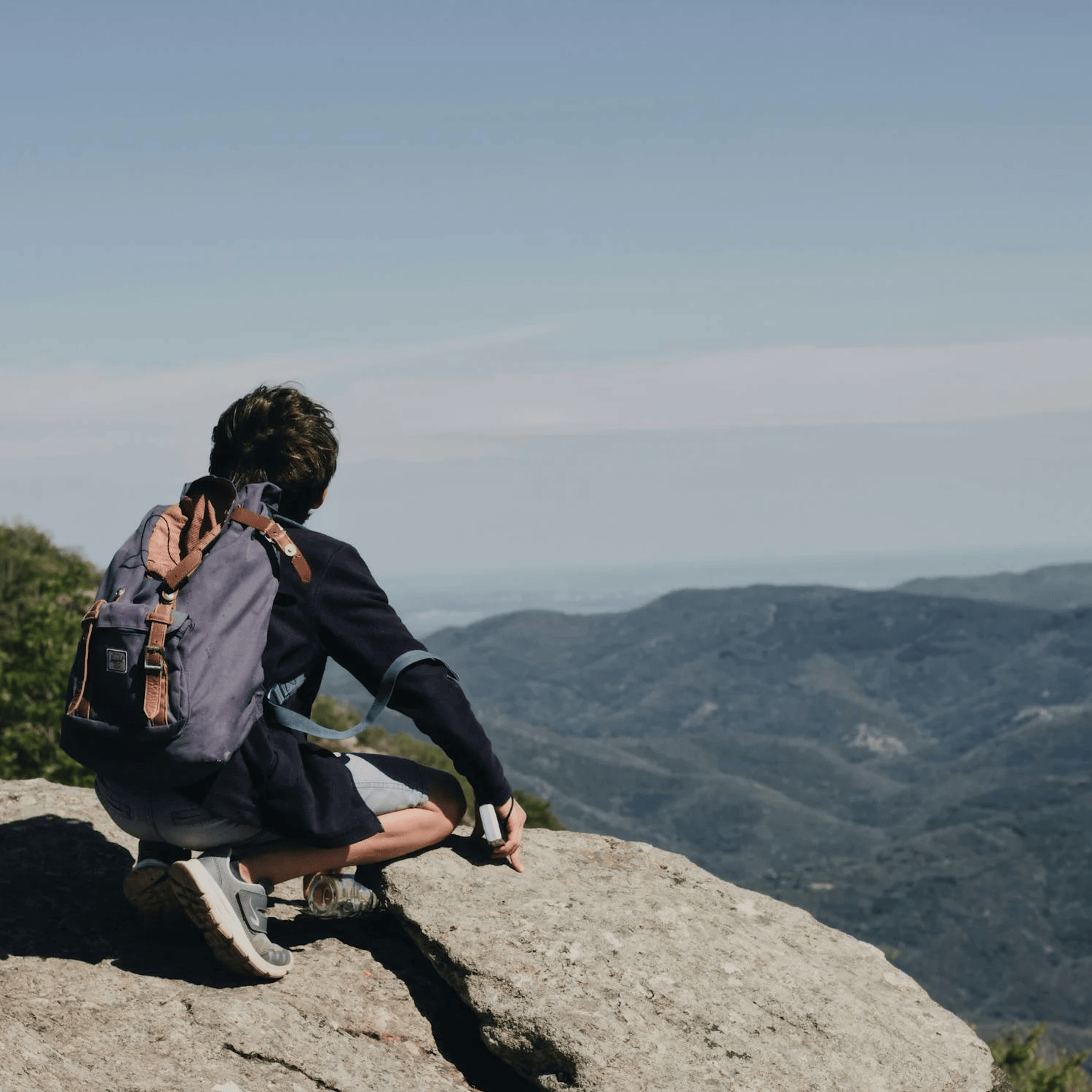 A man sititng on a rock on  a hilltop looking at the mountains in front of him