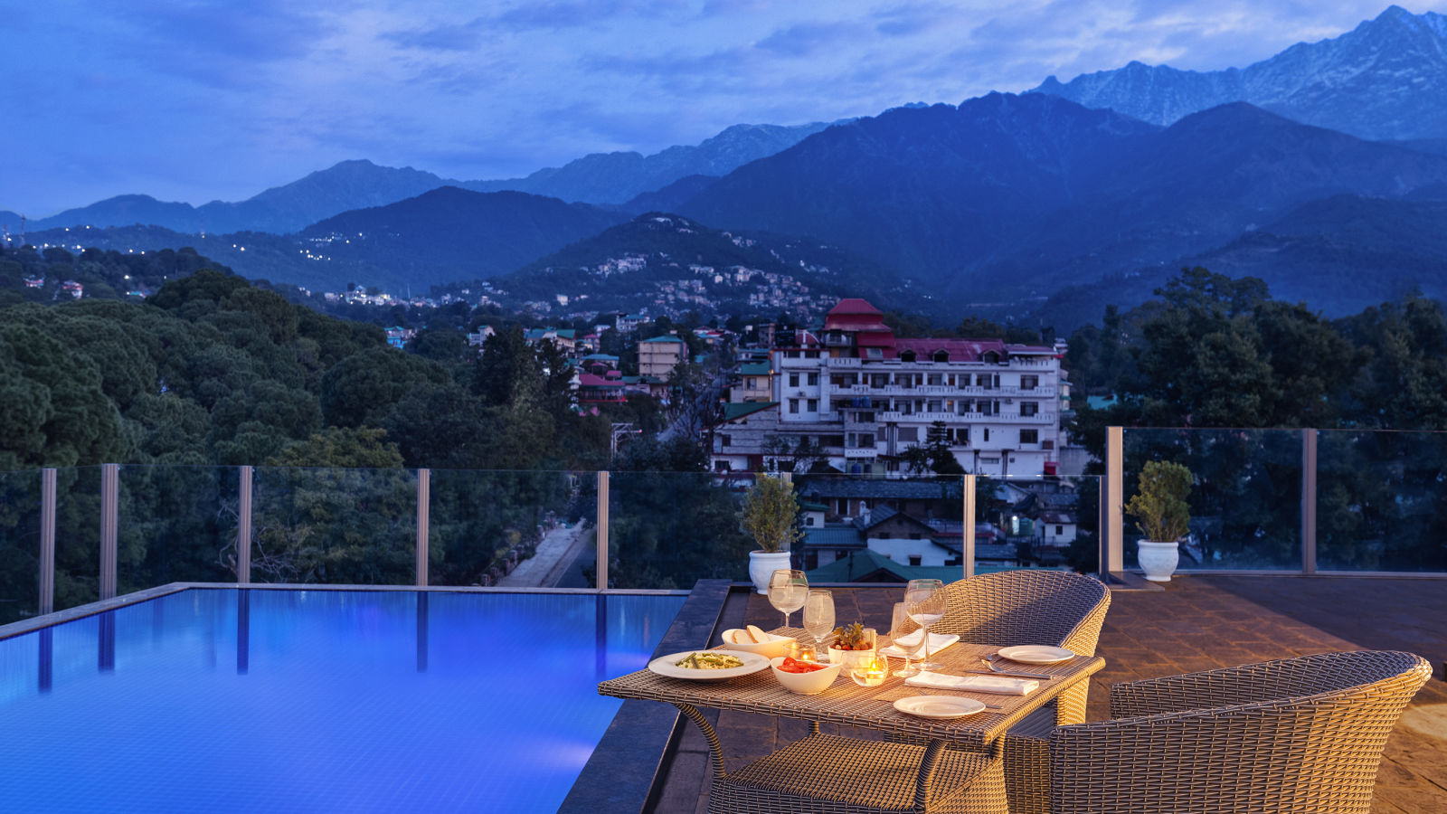 Rooftop pool lined with dining set up on the side on a clear blue day with mountains in the backdrop