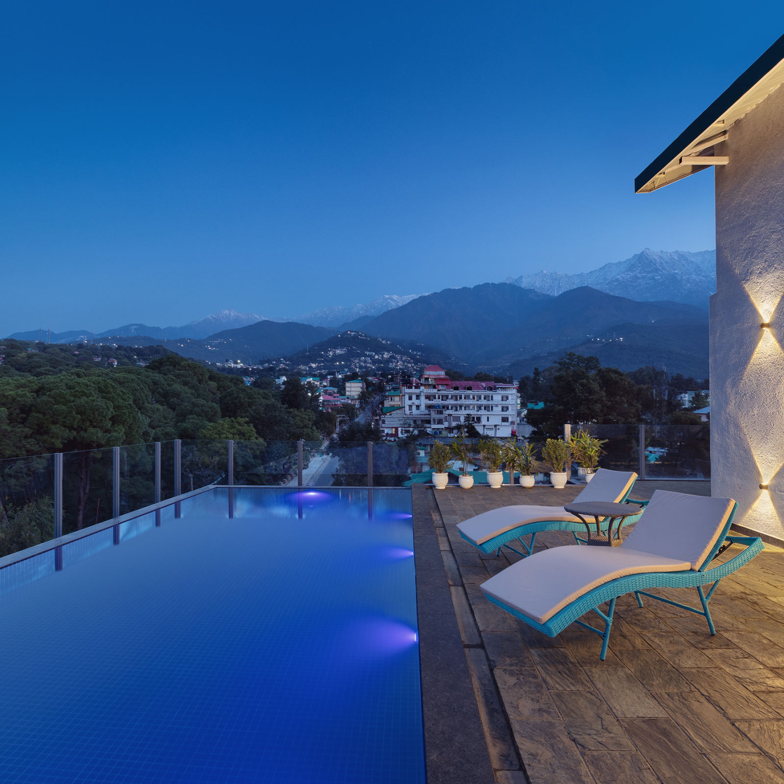 Roofrop pool lined with lounging chairs on a clear blue day with mountains in the backdrop