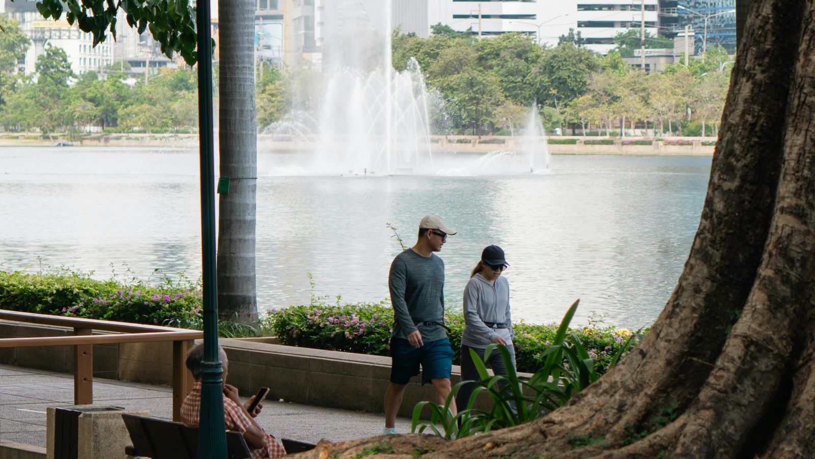 A couple walking on a pathway next to a fountain with trees in the foreground