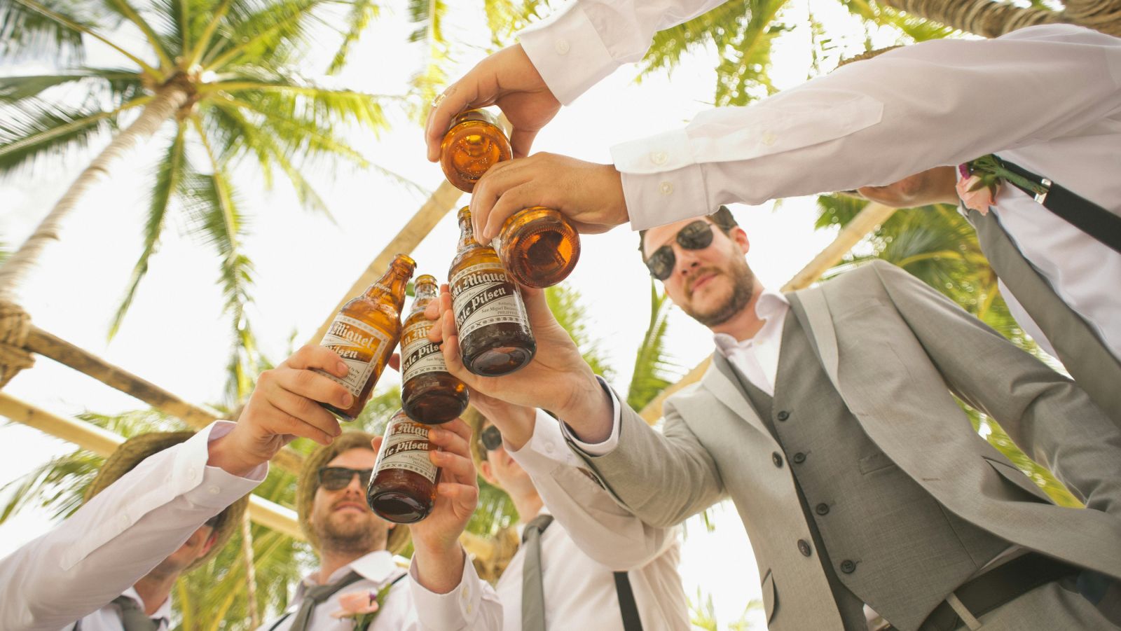 a group of guys toasting their drinks with palm trees above them