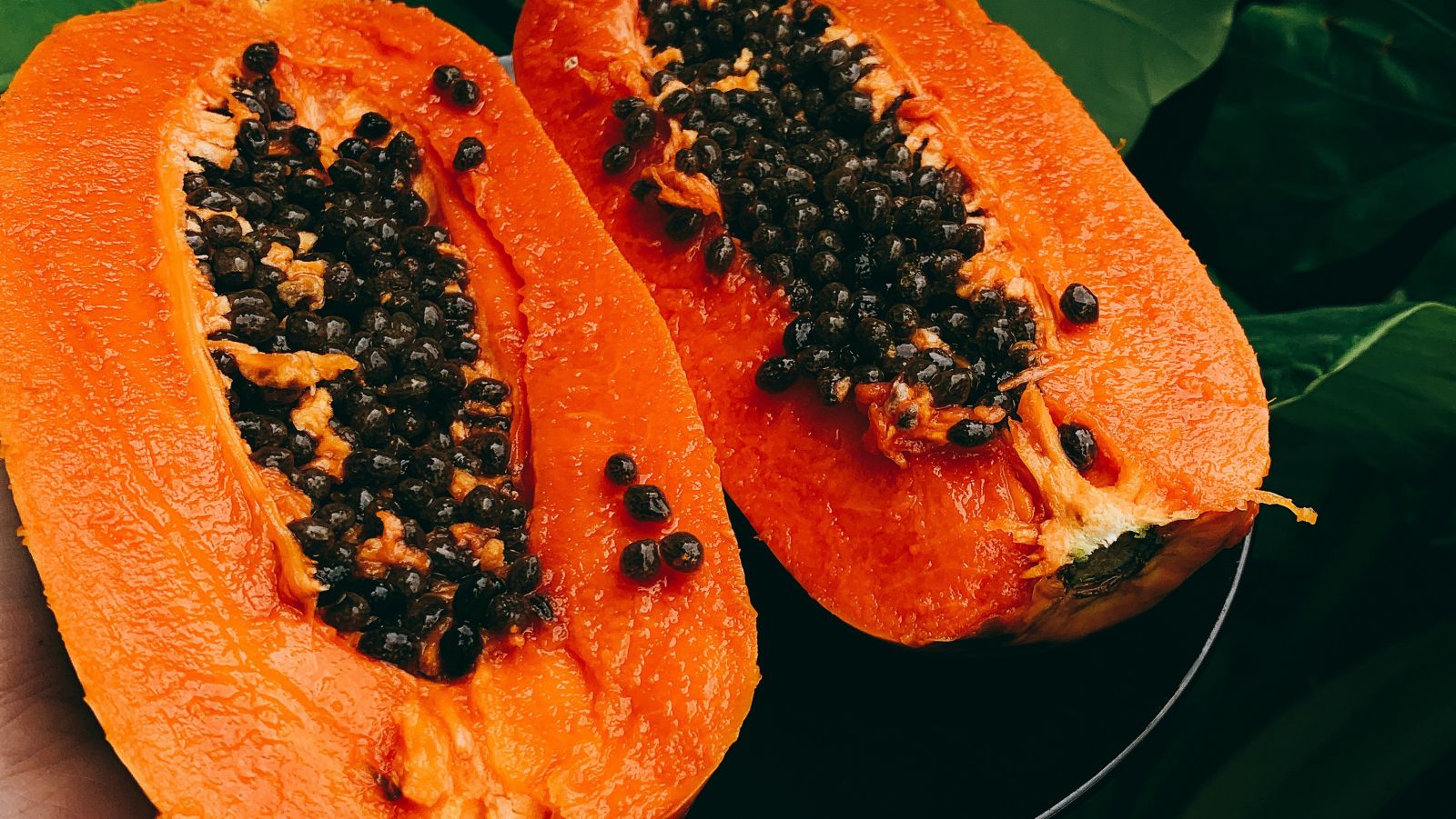 a papaya cut in half with its seeds intact and a banana leaf in the background