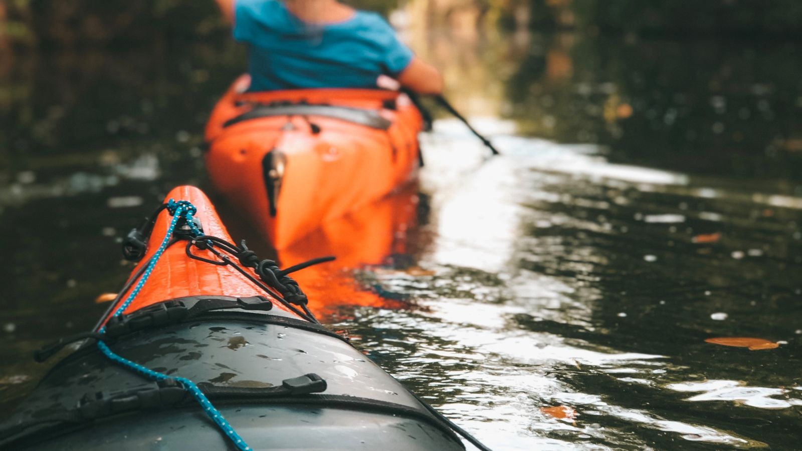 The bow of a canoe is visible in the foreground as a woman paddles away in her canoe in front of it - kayaking in Kumarakom