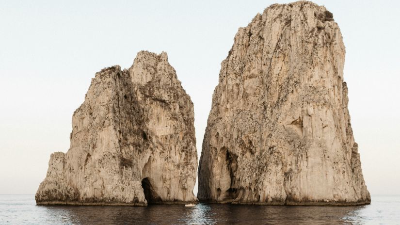 Two towering rock formations rise from the sea, with a natural arch in one of them.