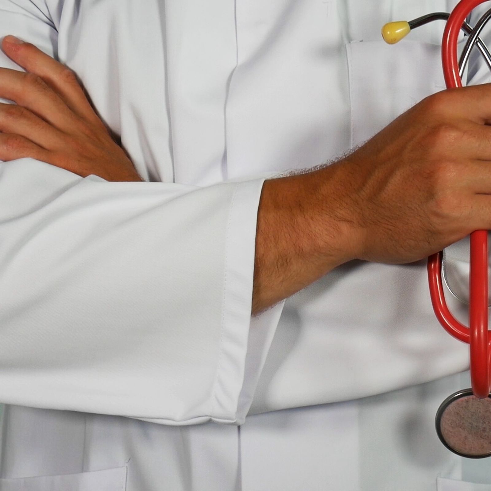 A doctor with folded hands, holding a stethoscope and wearing a white gown