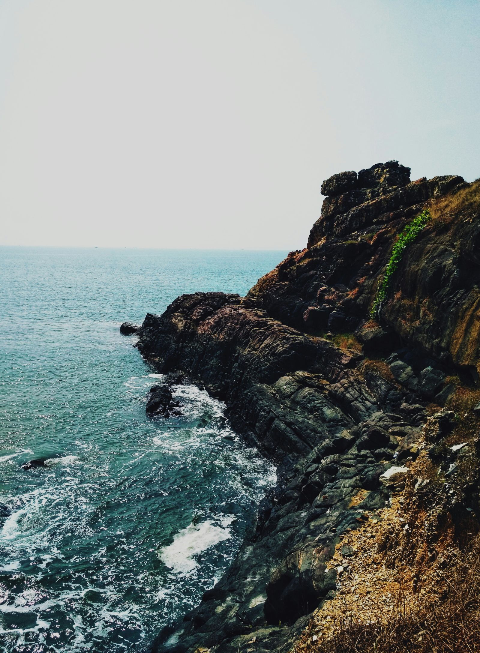 A far out view of a rocky cliff with the sea next to it with water overlapping on the rocks