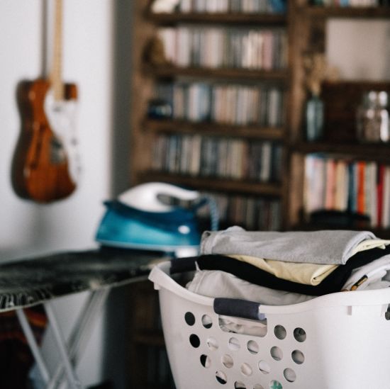 An image of a basket of fresh laundry placed in a room with a book shelf and guitar hanging on the wall