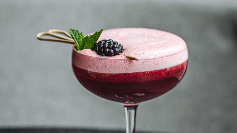 a cocktail garnished with a blackberry and mint leaves 