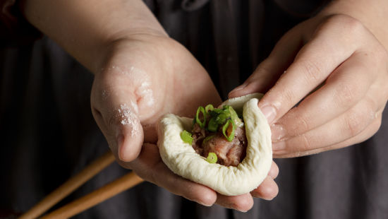 a chef showing how to prepare momo dumplings with a pair of chopsticks next to him and a few dough balls in front