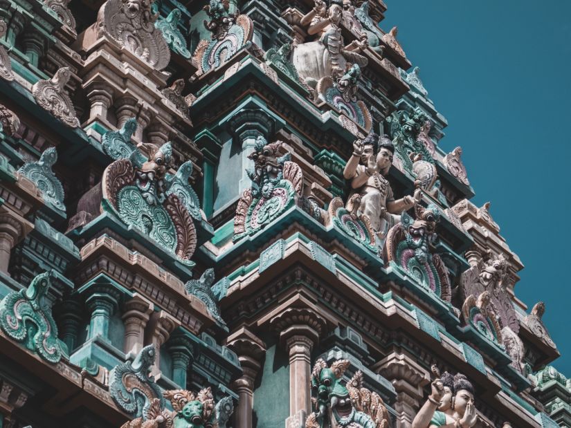 a far out image of many deities carved on the temple roof with blue sky in the background