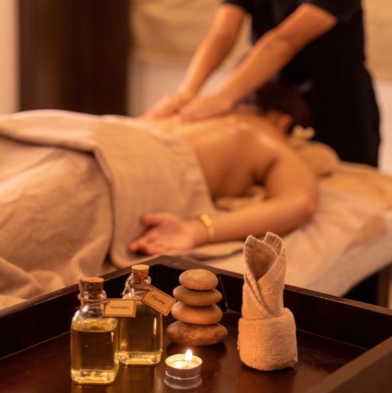 A woman getting a massage from a masseuse with massage oils in the foreground - The Ananta Udaipur