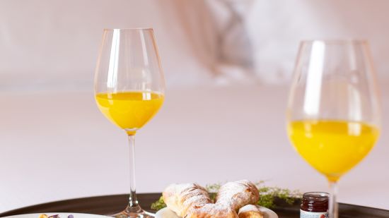 a tray kept on a bed with breakfast items on it and glasses of juices