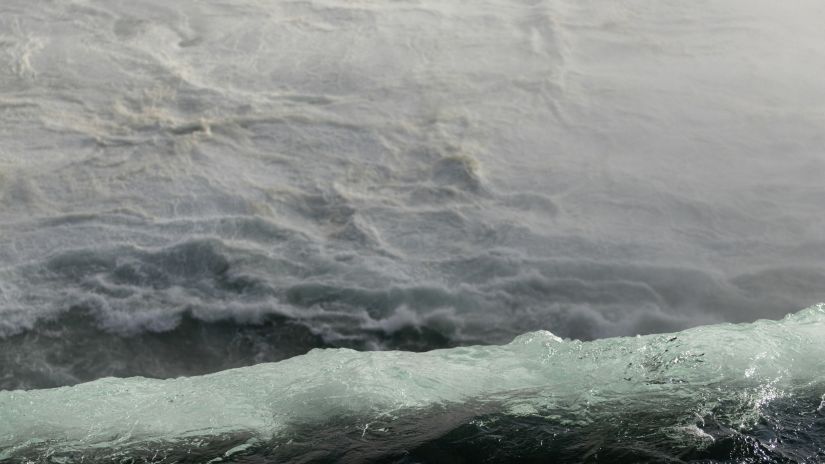 A close-up of water gushing over the edge of a waterfall, creating a misty spray