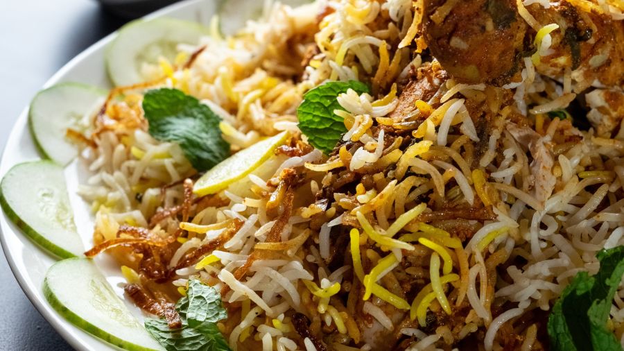 Biryani served on a white ceramic plate sided with raitha and gravy