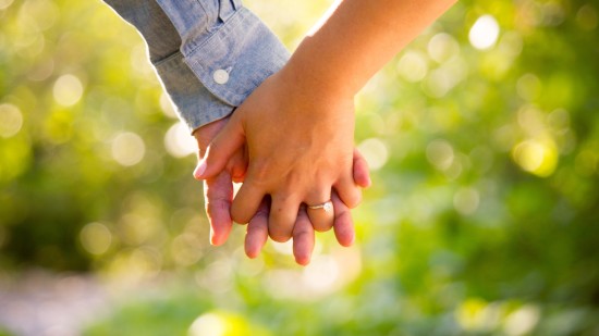 a close up image of a Couple holding hands with the background blurred