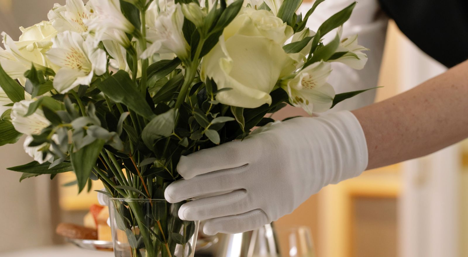 A waiter arranging a vase of white flowers on a table in a luxurious dining setting