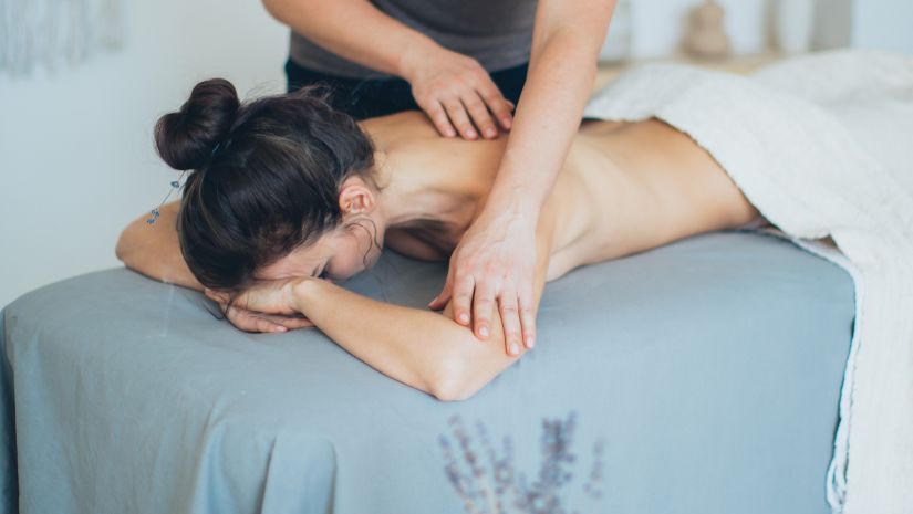 a masseur massaging a woman who is topless lying down on a massage table