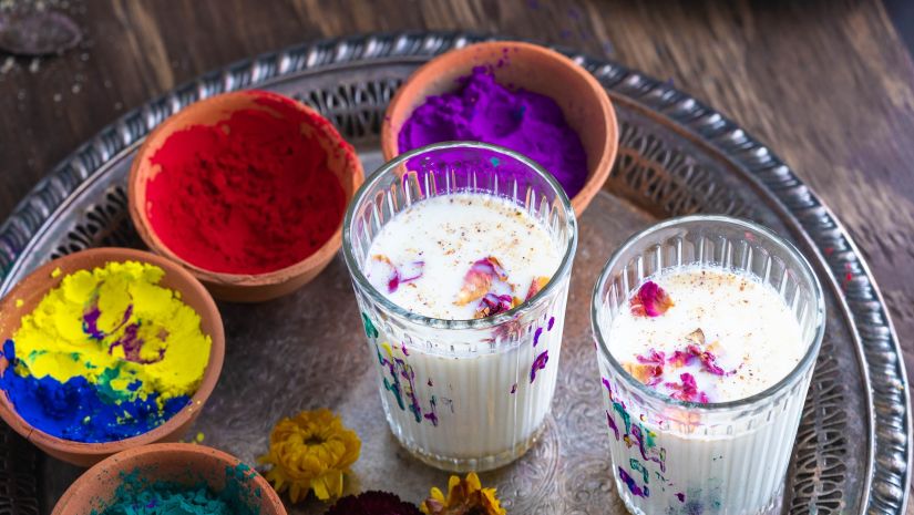 Image of multiple bowls containing gulal along with two glasses containing a milk based drink