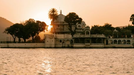 an overview of a lake in udaipur with trees and the setting sun in the background